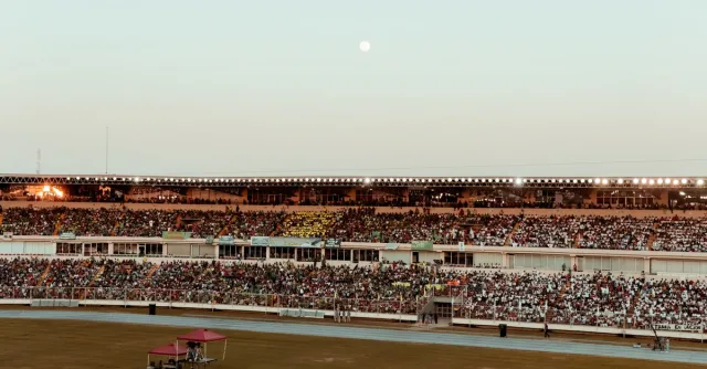 A bustling crowd fills the stadium under a clear evening sky, creating a vibrant atmosphere.