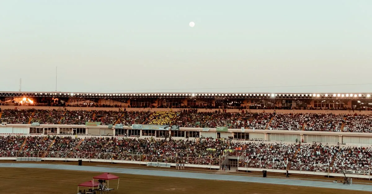 A bustling crowd fills the stadium under a clear evening sky, creating a vibrant atmosphere.