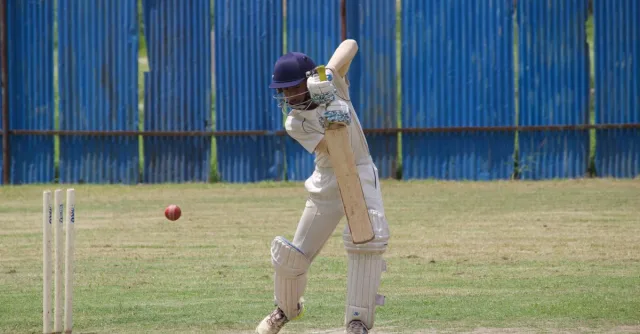 Cricket player in action, batting on a grass field in Gahunje, India.