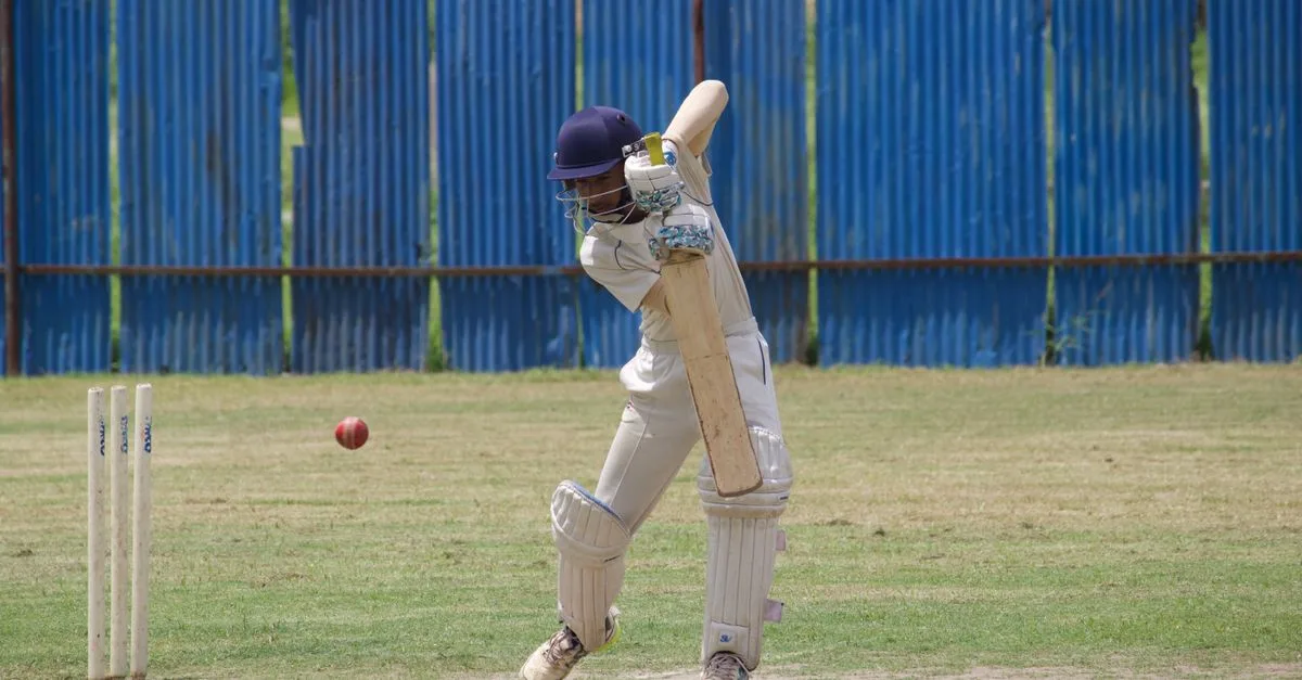 Cricket player in action, batting on a grass field in Gahunje, India.