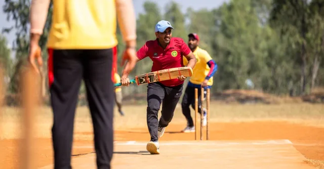 Dynamic scene of a cricket player running between wickets outdoors.
