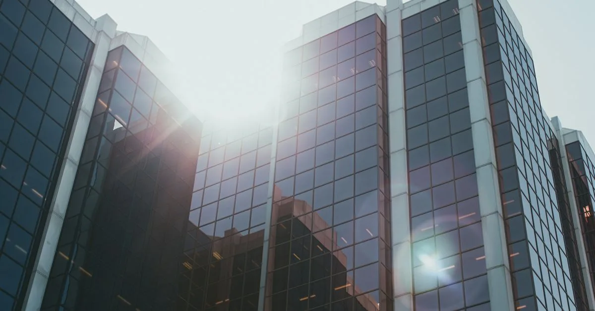 Low angle view of a modern glass skyscraper with sunlight reflecting off the facade.