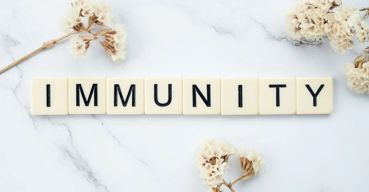 Elegantly arranged scrabble tiles spelling 'immunity' on a marble background with white flowers.