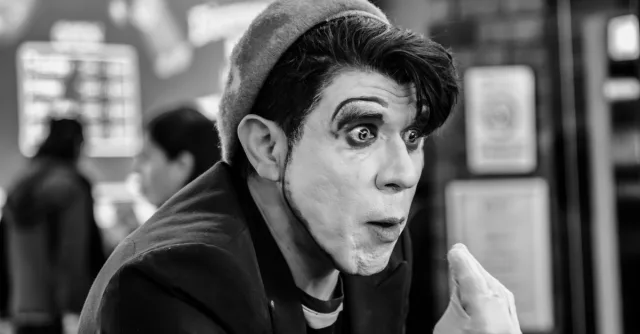 A captivating black and white portrait of a mime artist performing indoors, showcasing expressive facial expressions and makeup.