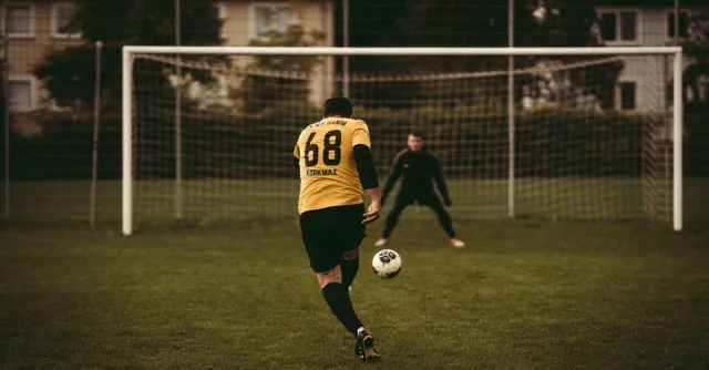 A soccer player takes a decisive penalty kick aiming to score against the goalkeeper.