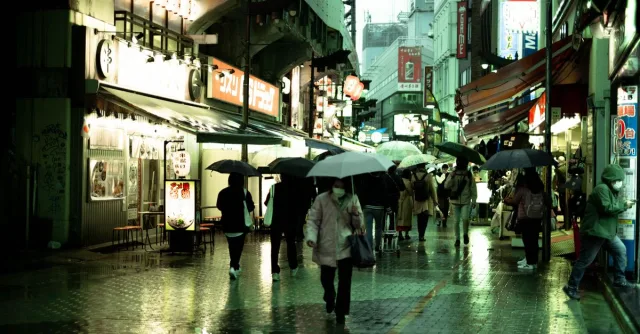 Photograph of a rainy street in Tokyo, Japan, with pedestrians under umbrellas.