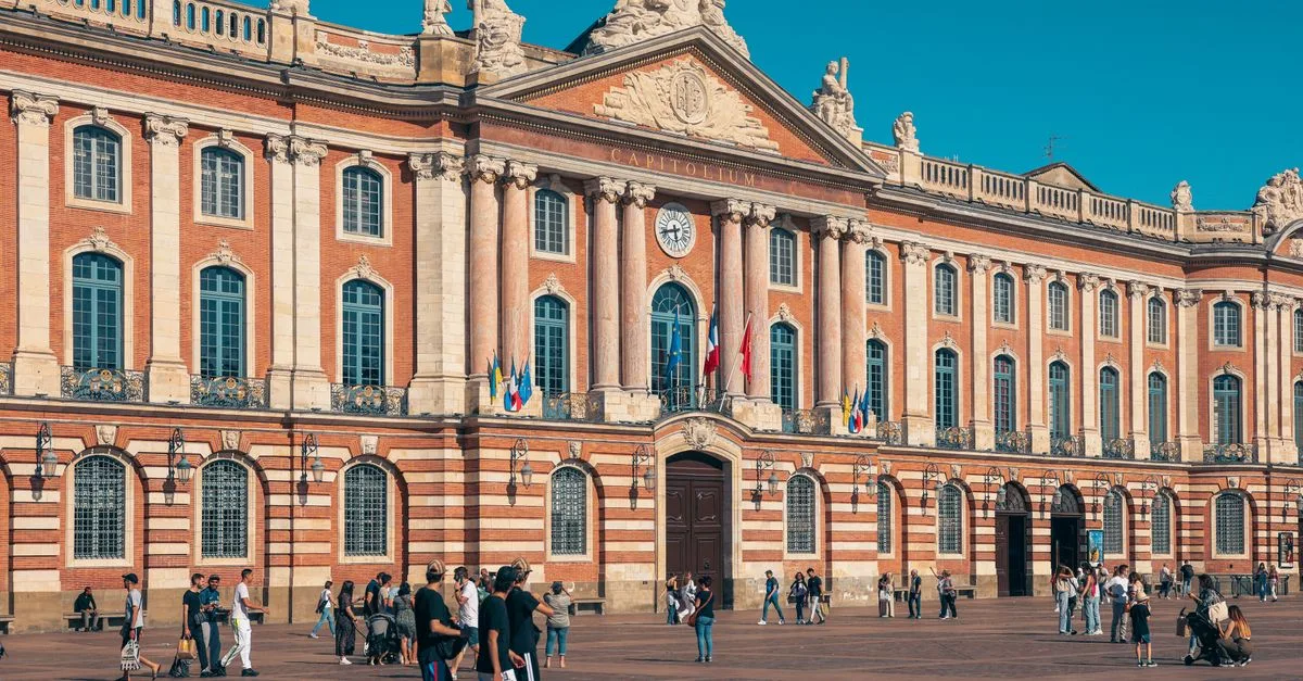 The iconic Capitole de Toulouse with people enjoying the sunny plaza in France.