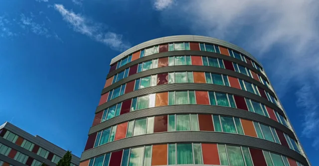 A modern curved building with colorful panels against a blue sky, showcasing urban architecture.