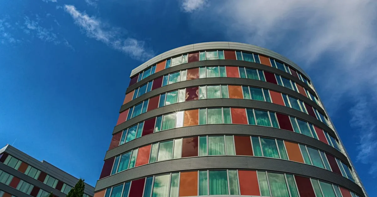 A modern curved building with colorful panels against a blue sky, showcasing urban architecture.
