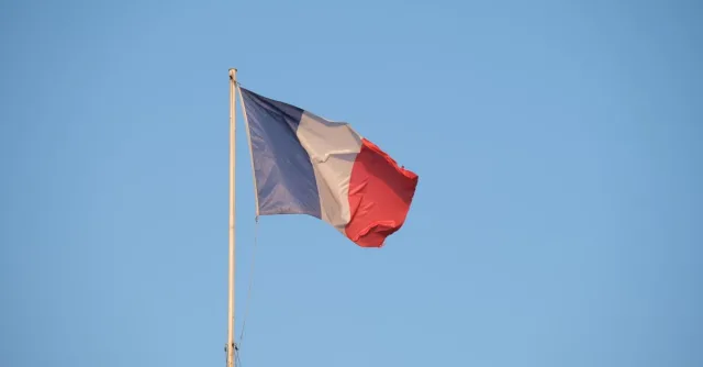 The French national flag waving on a flagpole against a clear blue sky.