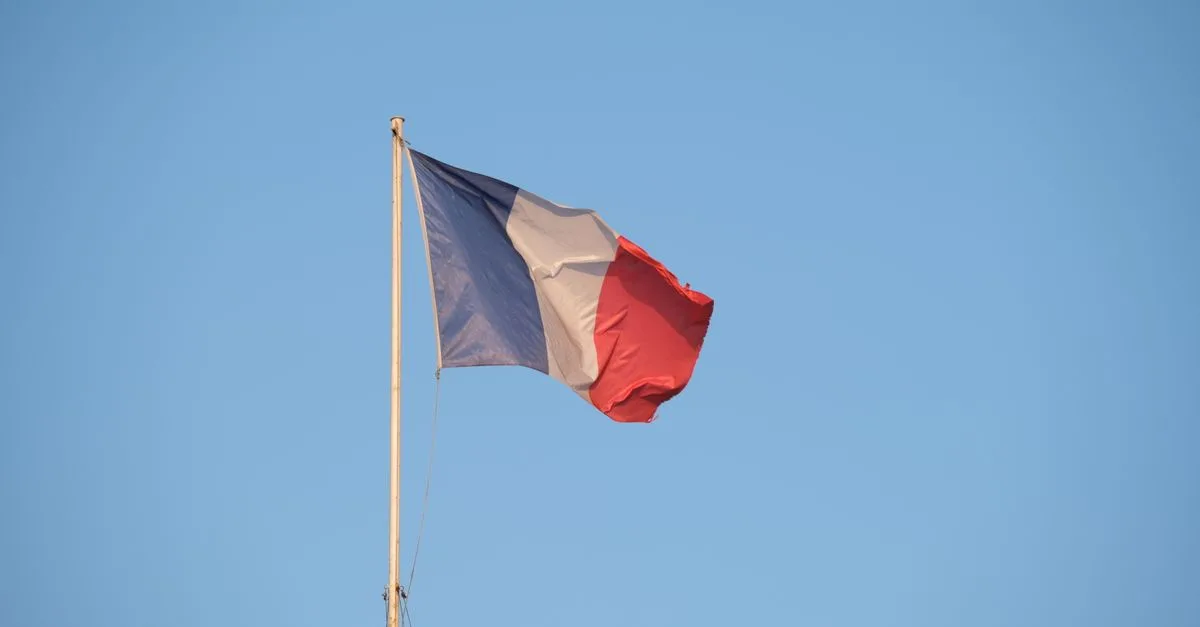 The French national flag waving on a flagpole against a clear blue sky.