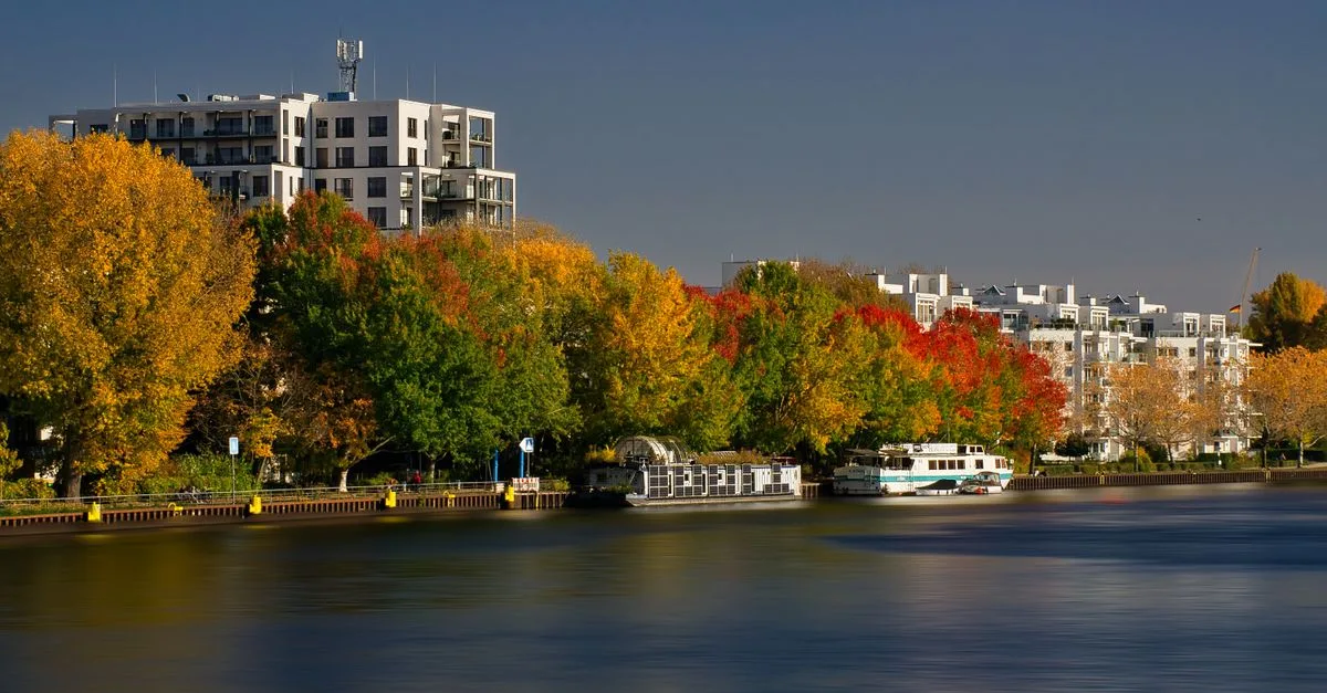 Scenic autumn view of a river with colorful trees and buildings in Berlin, Germany.