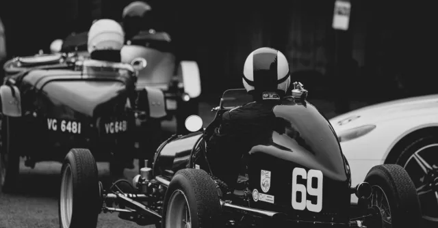 Black and white photo of a vintage car race with classic designs and helmets.