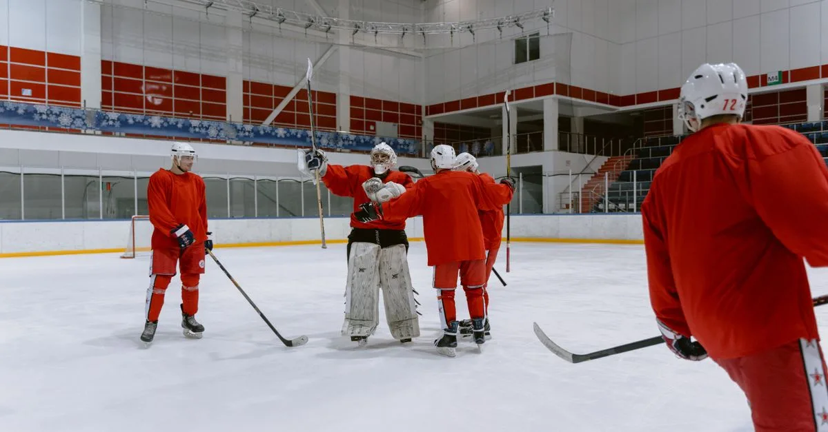 A group of ice hockey players in red jerseys celebrating on an indoor ice rink.