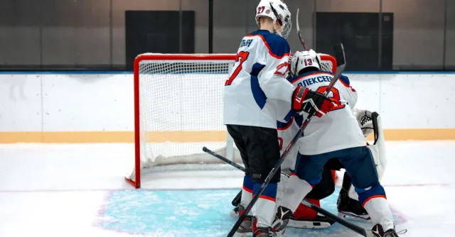 Ice hockey players compete intensely near the goal on a rink.
