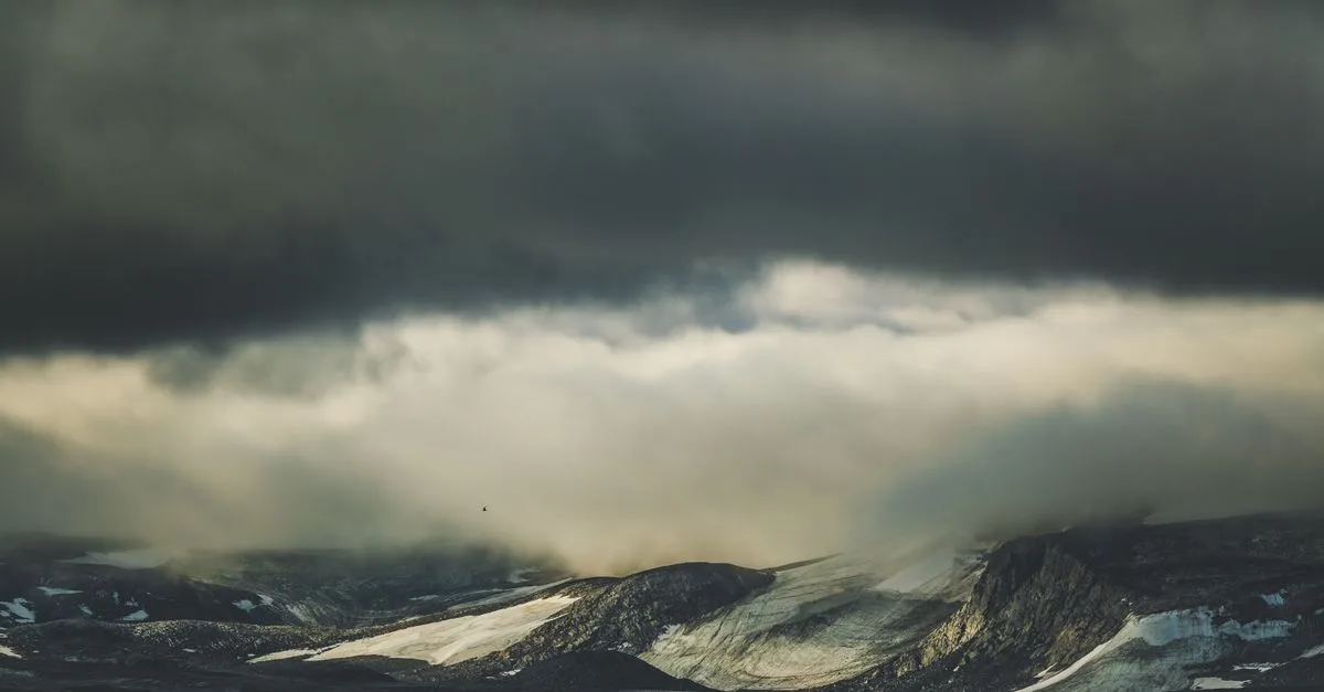 A moody landscape of mountains beneath a dramatic overcast sky full of thick clouds.