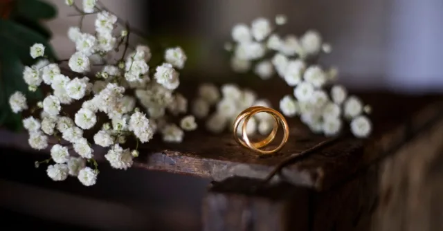 Beautiful gold wedding rings surrounded by white flowers on a rustic wooden surface. Perfect for wedding or romantic themes.