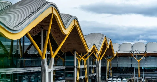 A striking view of a modern airport terminal with a distinctive wavy roof design and vibrant yellow supports.