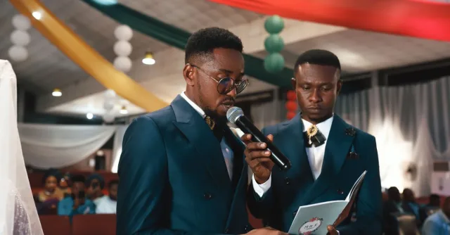 Two men in suits speaking at an indoor ceremony with elegant decor.