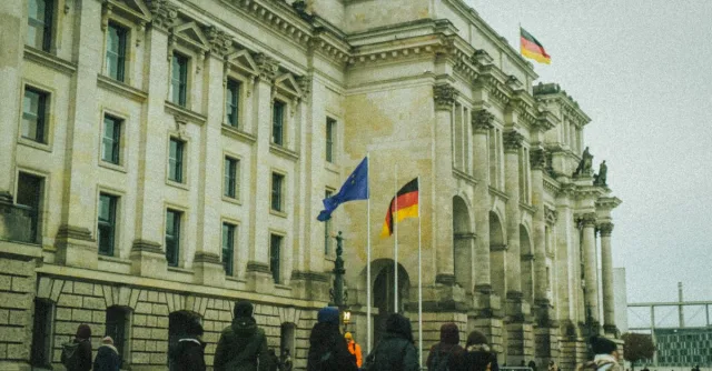 People walking outside a historic building in Germany with flags flying on a fall day.