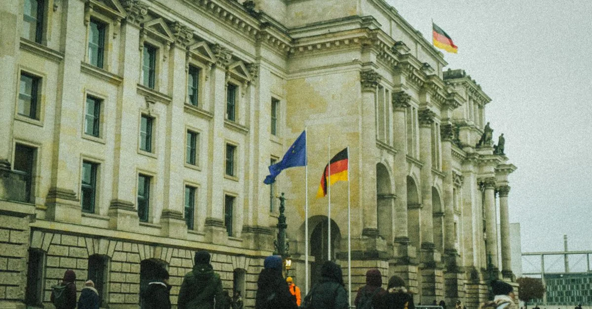 People walking outside a historic building in Germany with flags flying on a fall day.