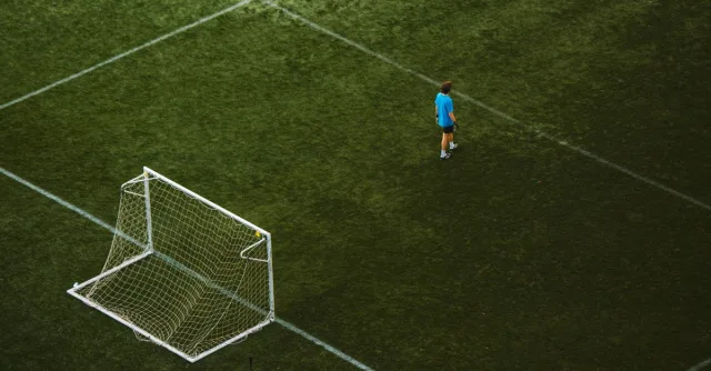 Aerial view of a lone soccer player near a goalpost on a grassy field.