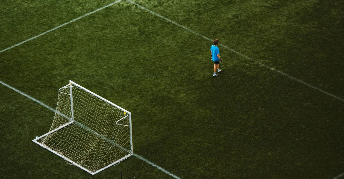 Aerial view of a lone soccer player near a goalpost on a grassy field.