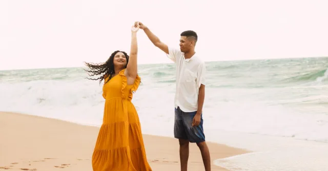 A joyful couple dances by the shore of Imbassaí Beach in Brazil, enjoying a bright day by the ocean.