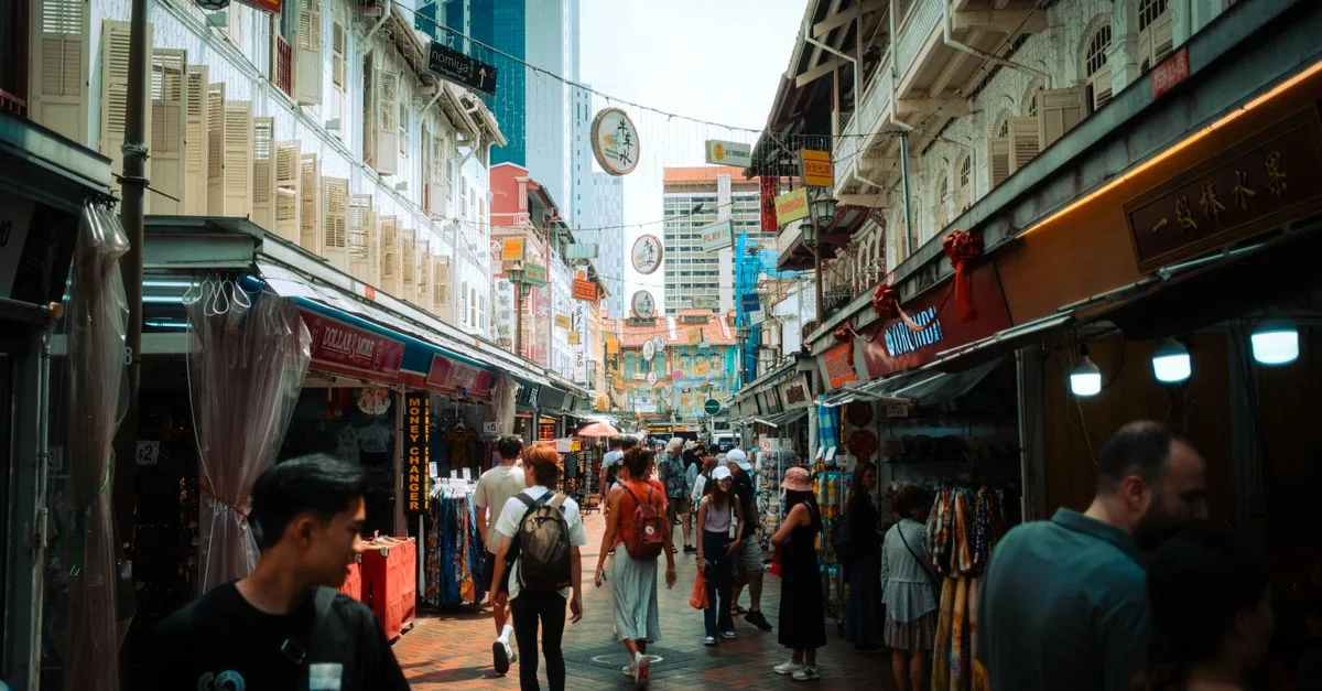 Vibrant street market in Singapore's Chinatown with tourists exploring shops and stalls under historic architecture.