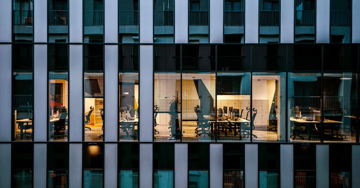 Illuminated office inside a modern glass building exterior, showcasing architecture and workspace design.