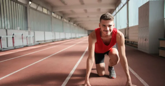 Male athlete in red top preparing for a sprint on an indoor track, showcasing determination and focus.