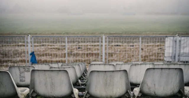 Desolate grandstand with empty seats facing a misty outdoor football field.