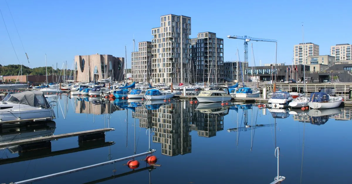 Tranquil harbor scene in Vejle, Denmark, showcasing boats, modern buildings, and a clear blue sky.