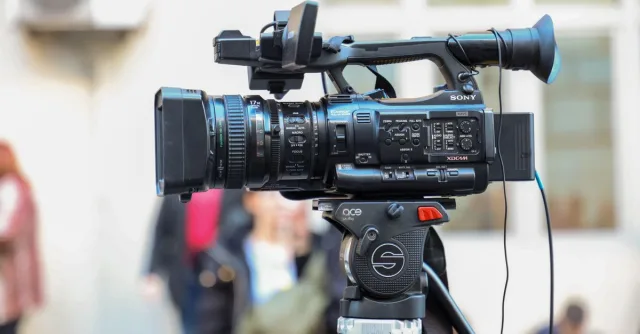 Close-up of a Sony video camera mounted on a tripod for outdoor filming.
