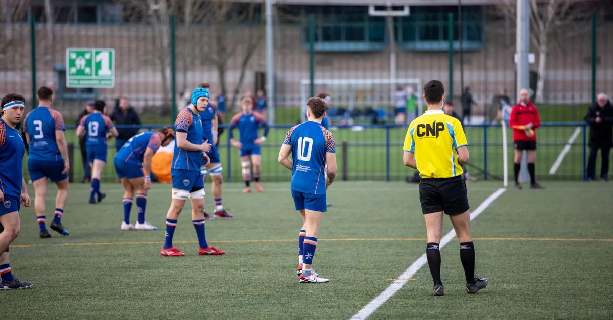 Action-packed rugby match with teams in blue and referee in a stadium, Manchester, UK.