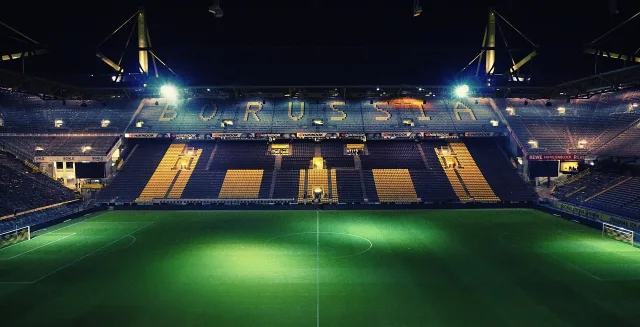 A professional football stadium under floodlights during an evening match.