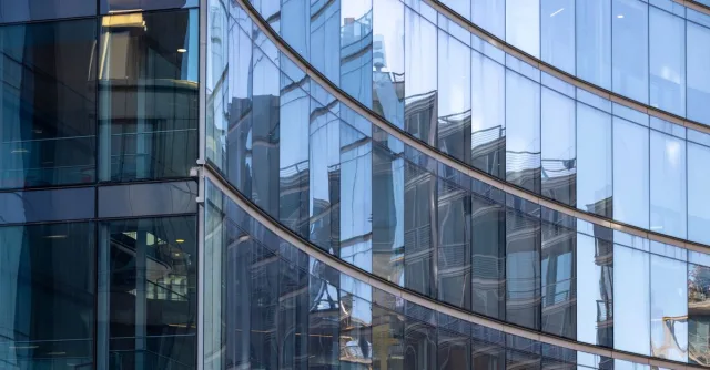 Close-up shot of a modern curved glass facade reflecting surrounding buildings in an urban setting.