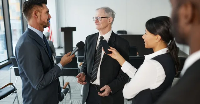 Journalists conduct an interview with a senior executive in a formal office setting.