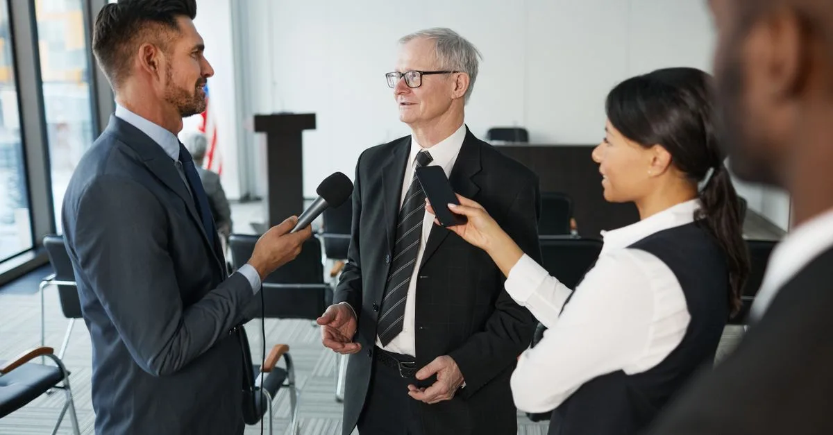 Journalists conduct an interview with a senior executive in a formal office setting.