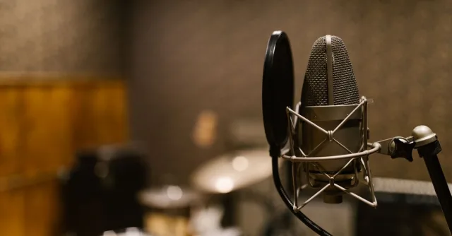 Close-up of a condenser microphone with a pop filter in a recording studio setting.