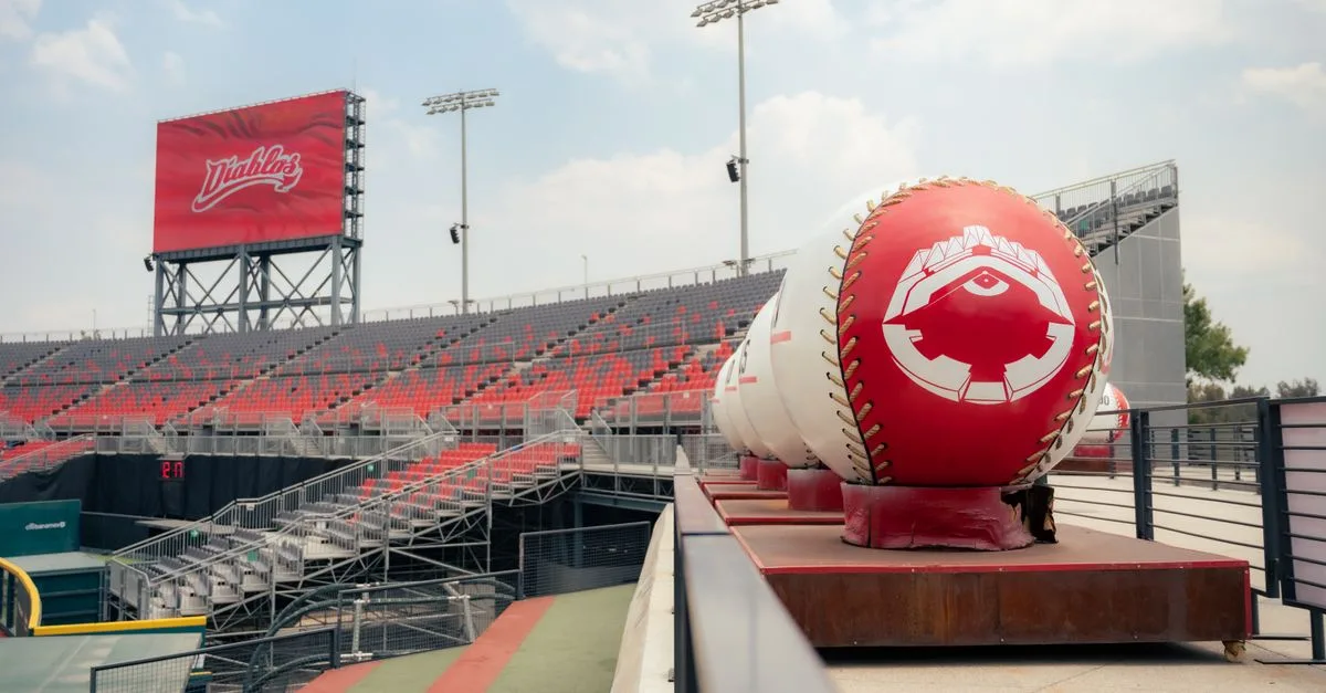 A view of an empty stadium with oversized baseball decorations under a clear sky.