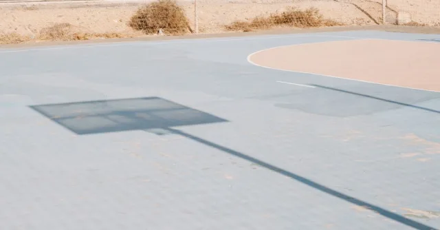 Empty basketball court with a shadow of hoop, outdoor scene on a sunny day.