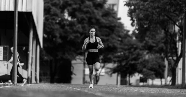 A young woman runs energetically outdoors, captured in a dynamic black and white photo.