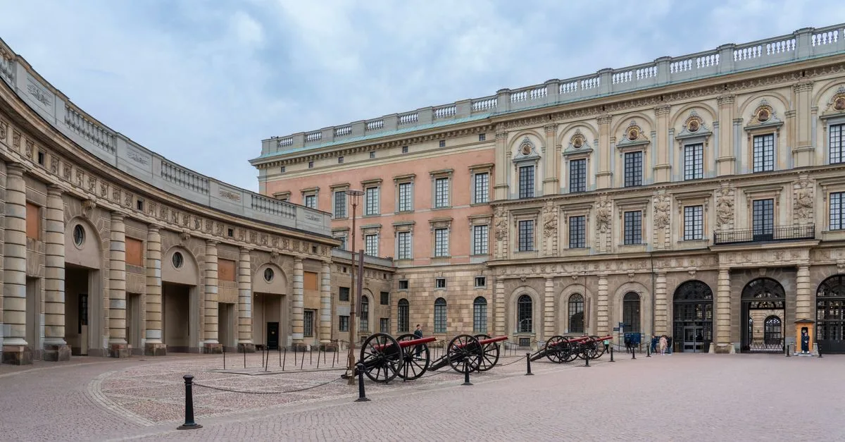 View of a historic building with cannons in a spacious stone courtyard under a cloudy sky.