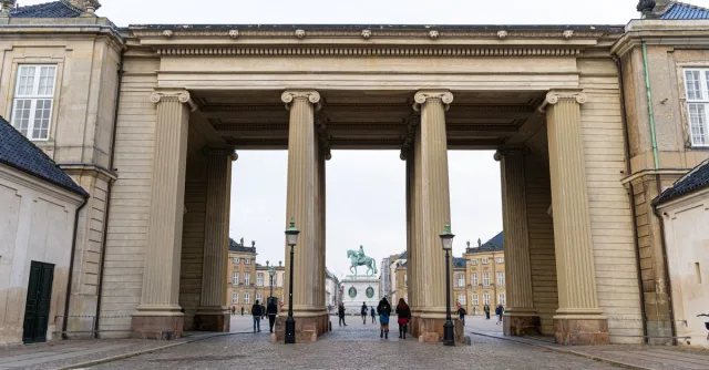 Historic entrance of Amalienborg Palace in Copenhagen with cobblestone path and surrounding architecture.