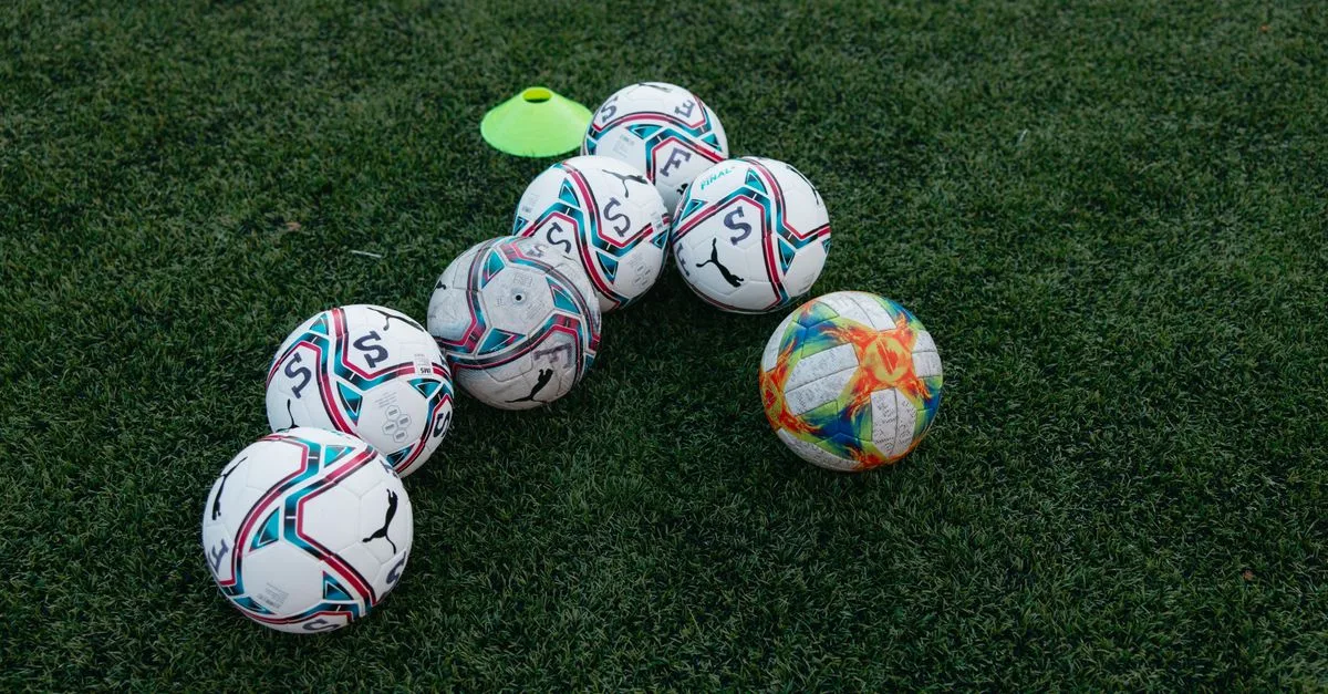 Group of soccer balls on a green grass field with a training cone, perfect for sports themes.