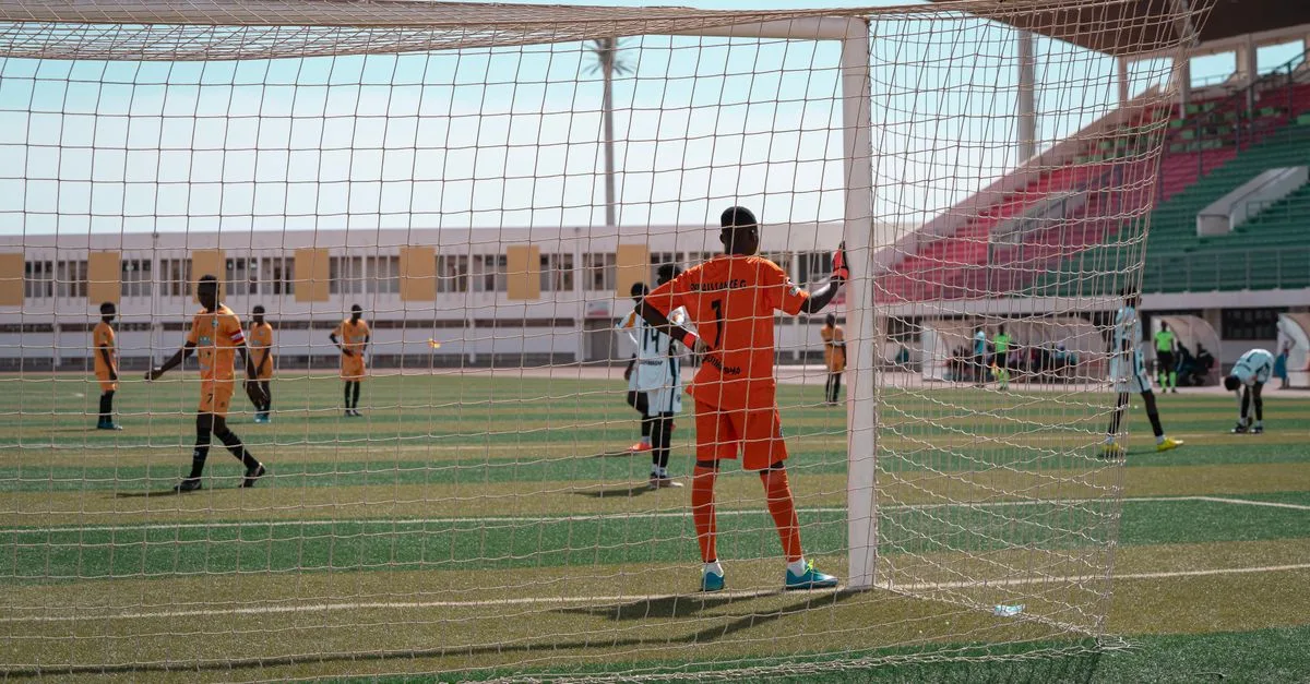 Soccer players in action during a competitive match, focusing on the goalkeeper's stance.