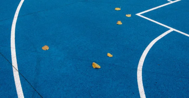 Vibrant blue sports court with white lines and scattered yellow leaves, showcasing abstract patterns.