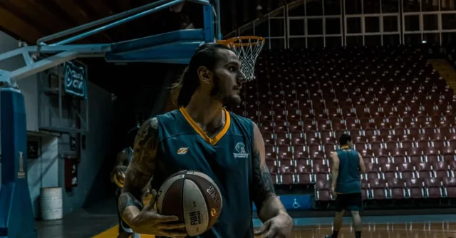 Male basketball players training and practicing in an indoor gym with basketballs and hoops.