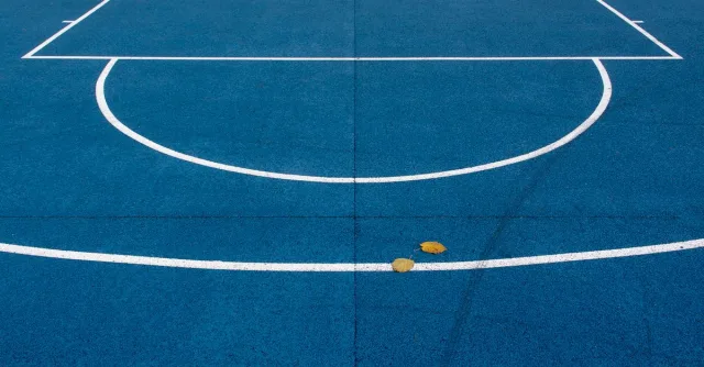 An empty blue basketball court with white lines and leaves on the surface.